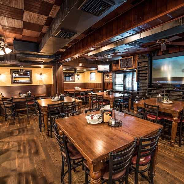 Interior of Bailey's Smokehouse with wooden tables, chairs, and a large TV showing sports.