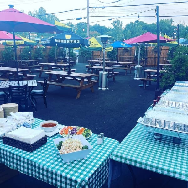 Bailey's Smokehouse outdoor patio with picnic tables, colorful umbrellas, and buffet tables with food.