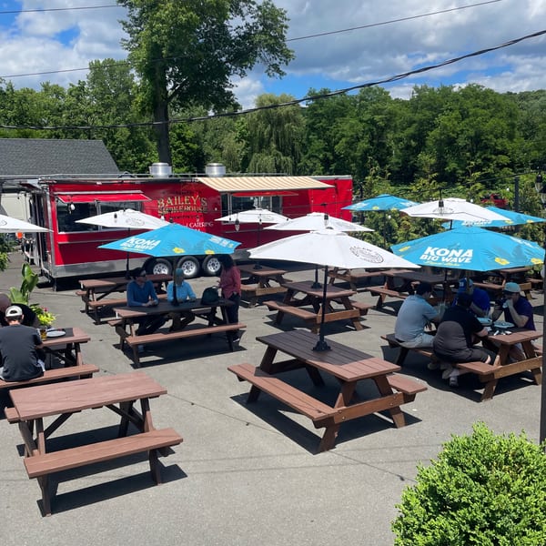Outdoor patio of Bailey's Smokehouse with picnic tables, umbrellas, and a red food truck.