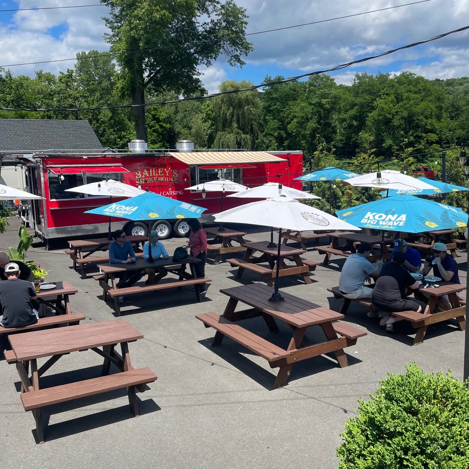 Outdoor patio of Bailey's Smokehouse with picnic tables, umbrellas, and a red food truck.