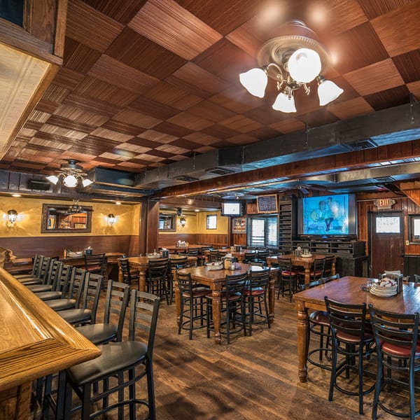 Interior of Bailey's Smokehouse, featuring wooden tables, chairs, a bar, and a large TV screen.