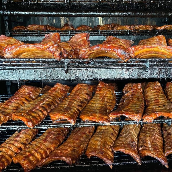 Rows of glistening, smoked ribs cooking on racks inside a dark, industrial smoker at Bailey's Smokehouse.