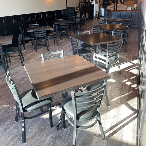 Empty dining room at Bailey's Smokehouse with dark wood tables and chairs, sunlit floor.