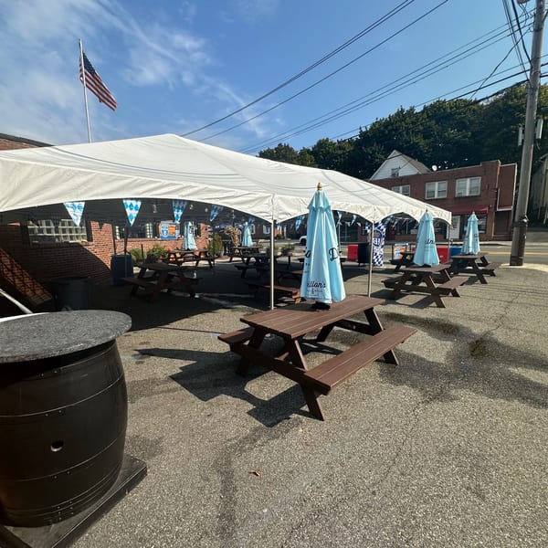 Outdoor patio at Bailey's Smokehouse with picnic tables under a large white tent and blue umbrellas.
