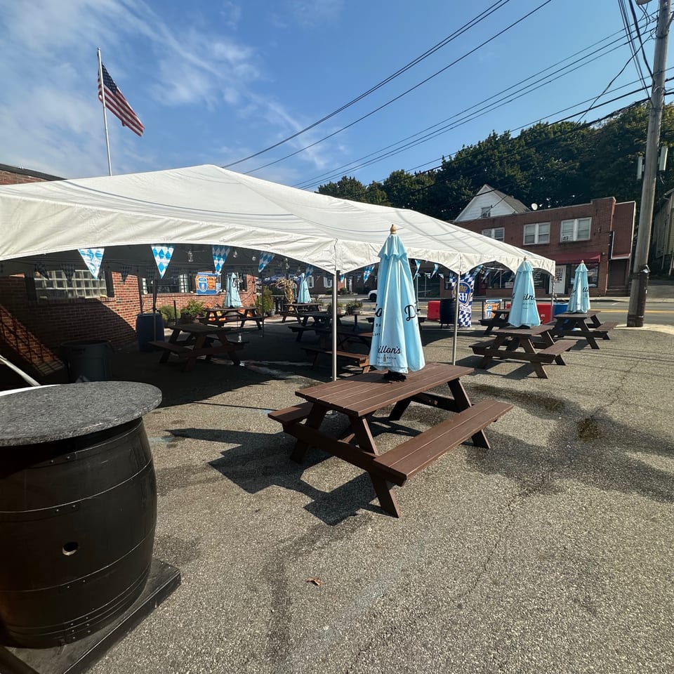 Outdoor patio at Bailey's Smokehouse with picnic tables under a large white tent and blue umbrellas.