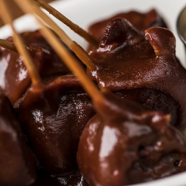 Close-up of several dark brown, glossy BBQ bites on skewers in a white dish.