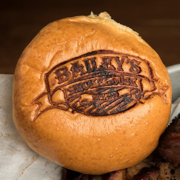Close-up of a Bailey's Smokehouse branded bun, lightly toasted, sitting atop barbecue meat.