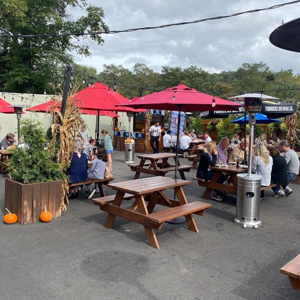 Outdoor patio at Bailey's Smokehouse with people dining at picnic tables under red umbrellas.