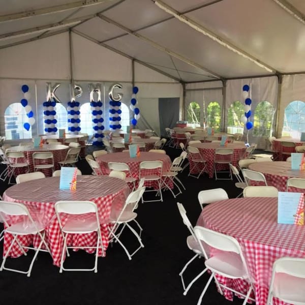 A large white tent with round tables covered in red and white checkered tablecloths, set for an event.