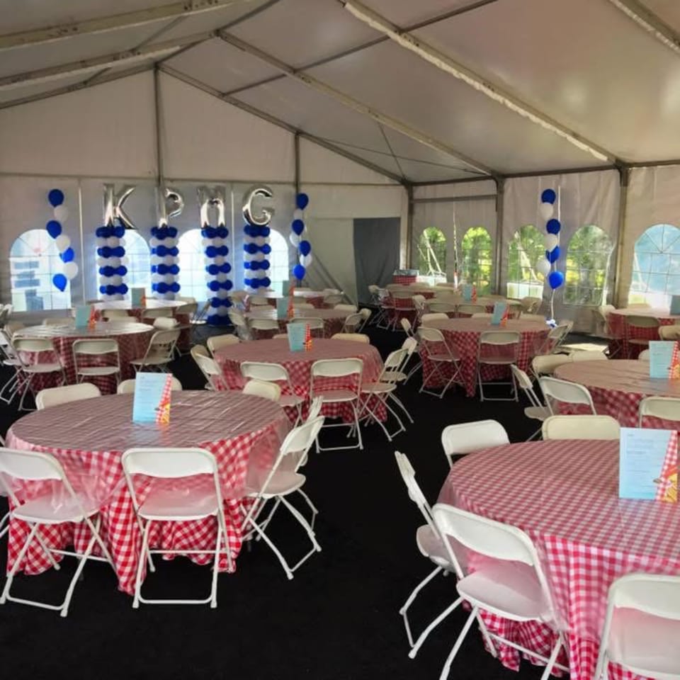 A large white tent with round tables covered in red and white checkered tablecloths, set for an event.