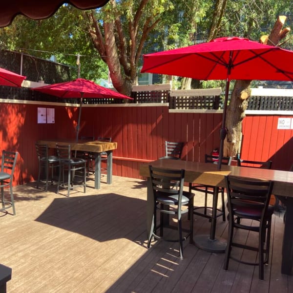 Outdoor patio at Bailey's Smokehouse with red umbrellas, wooden tables, and black chairs on a sunny day.
