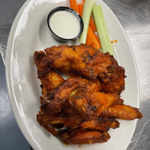 Bailey's Smokehouse BBQ chicken wings with ranch dressing, celery, and carrot sticks on a white plate.