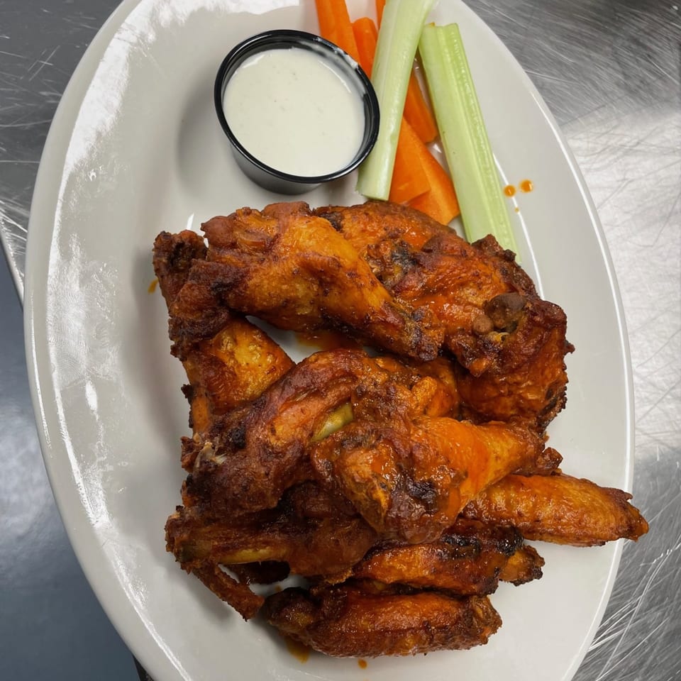 Bailey's Smokehouse BBQ chicken wings with ranch dressing, celery, and carrot sticks on a white plate.