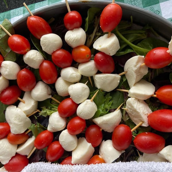 Caprese skewers with cherry tomatoes and mozzarella balls, arranged over a bed of green salad.