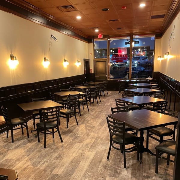 An empty dining room at Bailey's Smokehouse with dark tables and chairs, wood paneling, and sconce lighting.