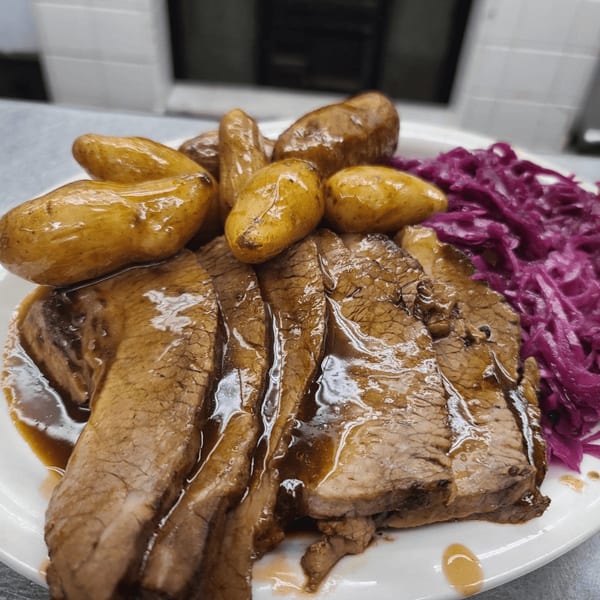 Sliced brisket with gravy, roasted baby potatoes, and purple cabbage on a white plate.