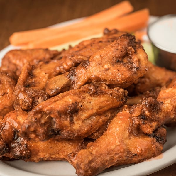 A plate of Bailey's Smokehouse BBQ chicken wings with celery sticks and ranch dressing.