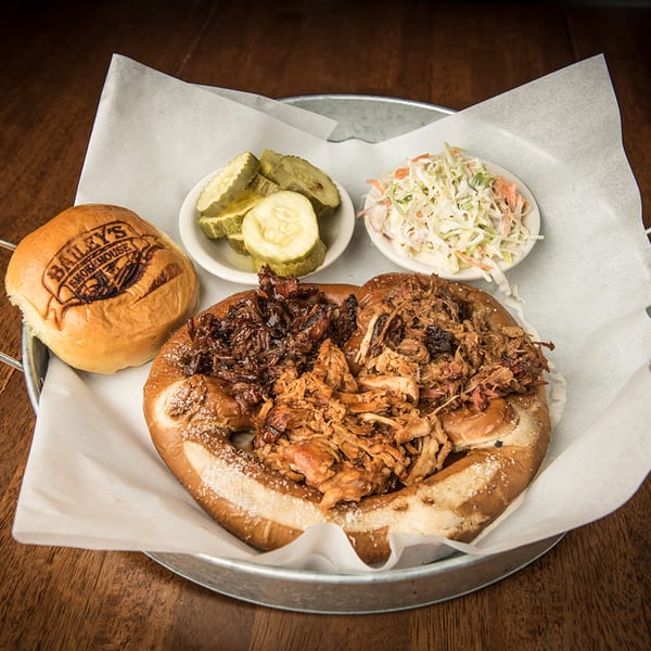 Bailey's Smokehouse BBQ platter with pulled pork, brisket, pretzel bun, pickles, and coleslaw.