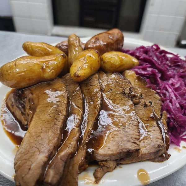 Sliced brisket with gravy, roasted potatoes, and red cabbage on a white plate at Bailey's Smokehouse.