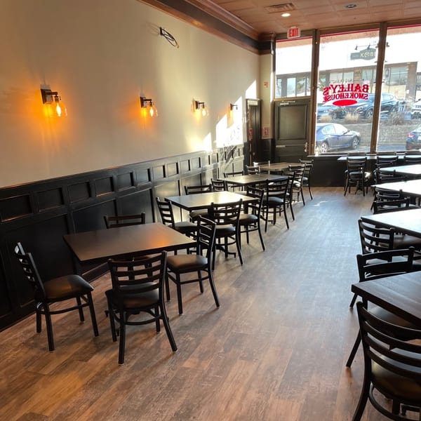 Interior of Bailey's Smokehouse dining room with empty tables and chairs, dark wainscoting, and large windows.