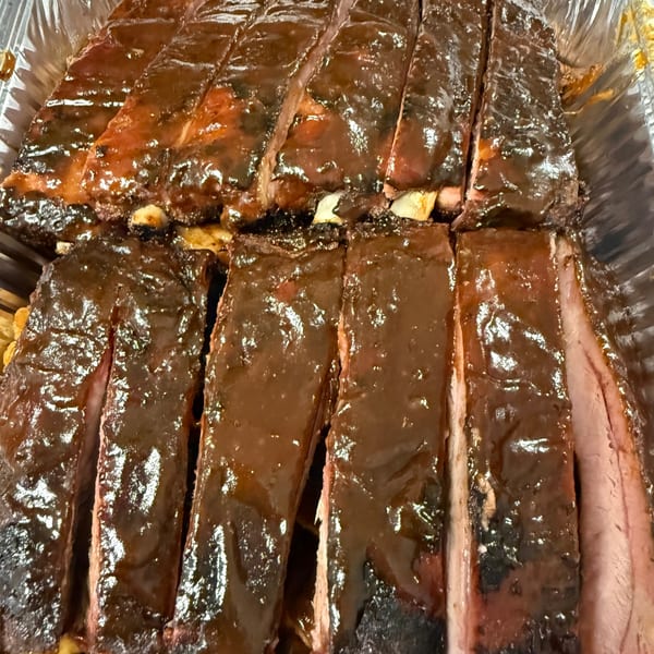 Close-up of glistening, saucy BBQ ribs, cut into individual portions, in a foil pan.
