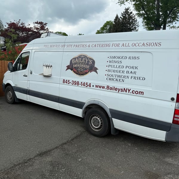 Bailey's Smokehouse catering van with menu items and contact information on its side.