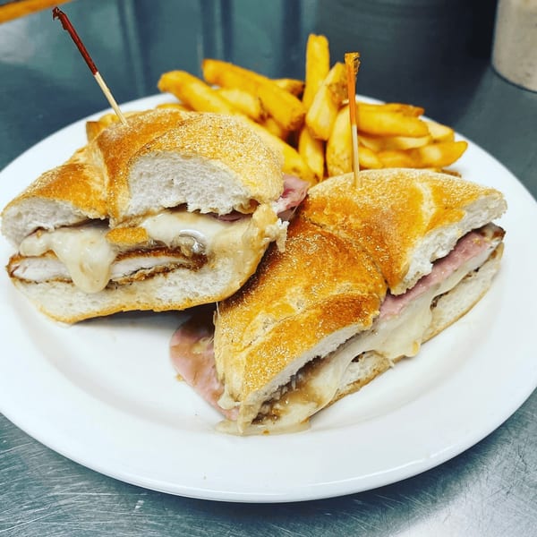 Two halves of a cheesy chicken sandwich with ham and fries on a white plate.