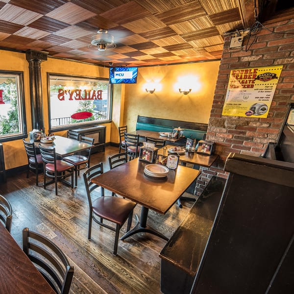 Interior of Bailey's Smokehouse, featuring wooden tables, chairs, booths, and a brick wall with a sign.