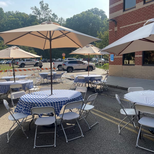 Outdoor patio dining area with blue and white checkered tables, white chairs, and umbrellas at Bailey's Smokehouse.