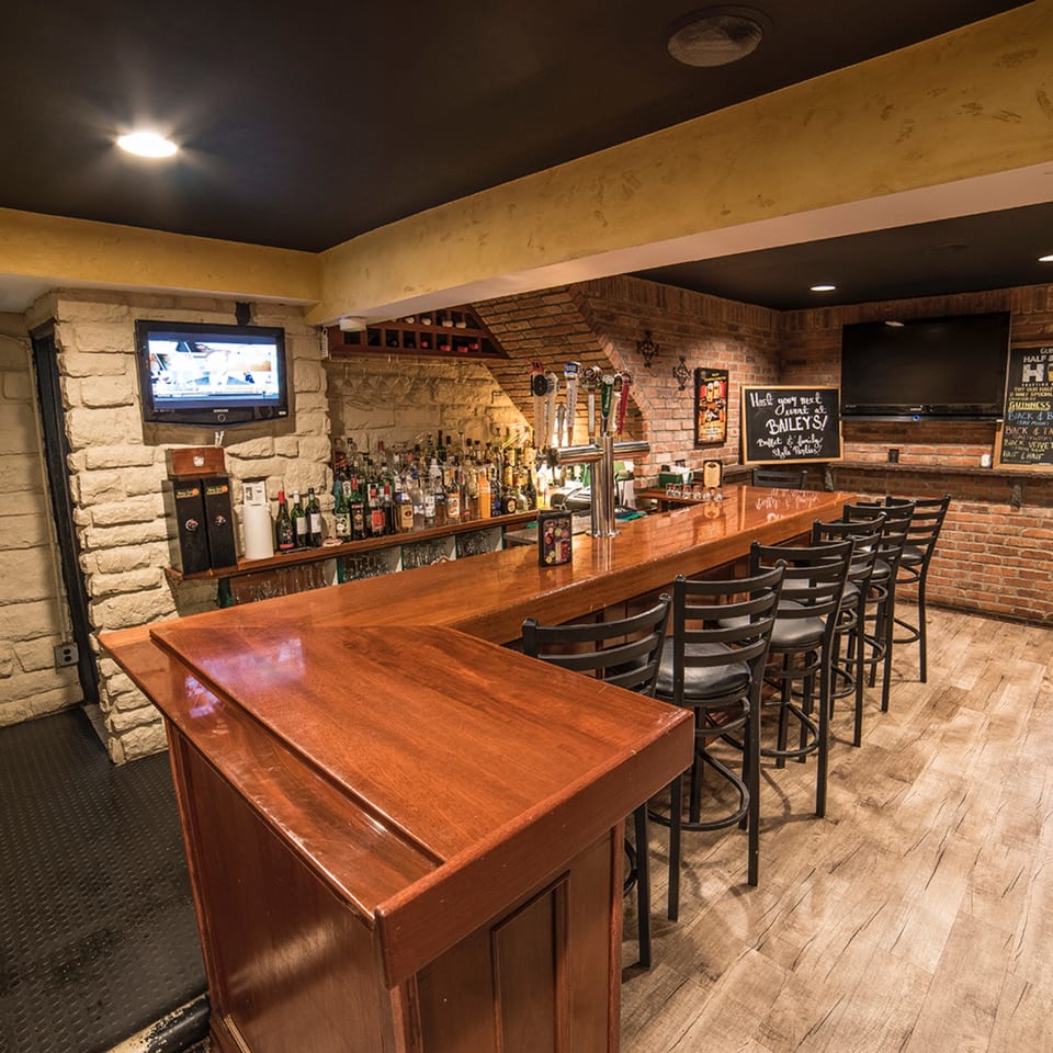 Bailey's Smokehouse bar with a long wooden counter, bar stools, brick walls, and multiple beer taps.