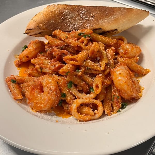 A plate of penne pasta with shrimp and calamari in red sauce, served with garlic bread.