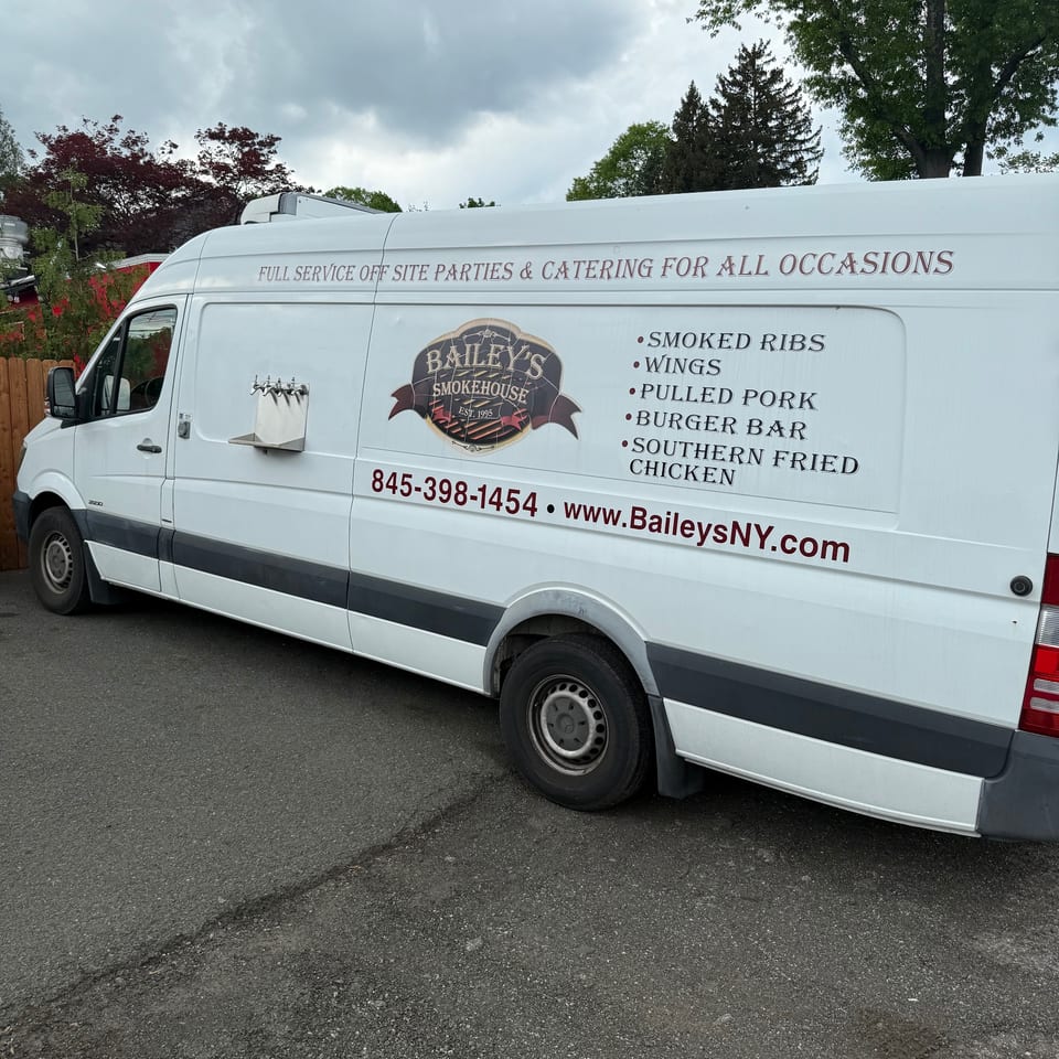 Bailey's Smokehouse catering van with menu items, contact info, and beer taps on the side.