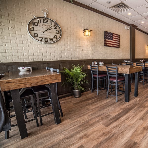 Interior of Bailey's Smokehouse with wooden tables, chairs, brick walls, a large clock, and an American flag.