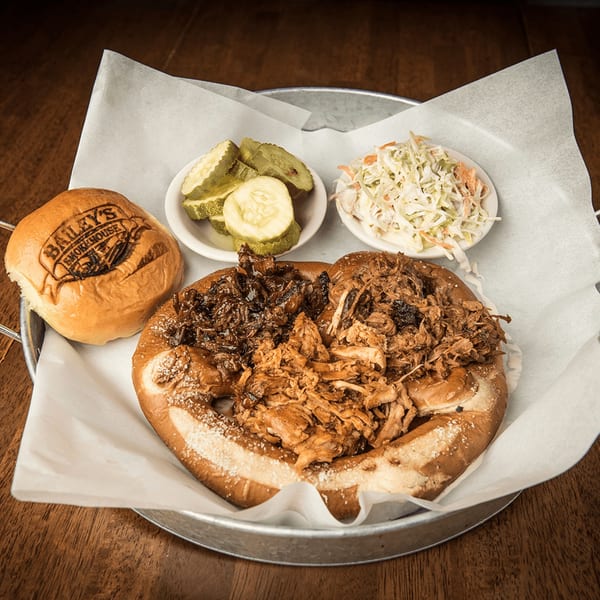 Bailey's Smokehouse BBQ platter with pulled pork, brisket, pretzel bun, pickles, and coleslaw.