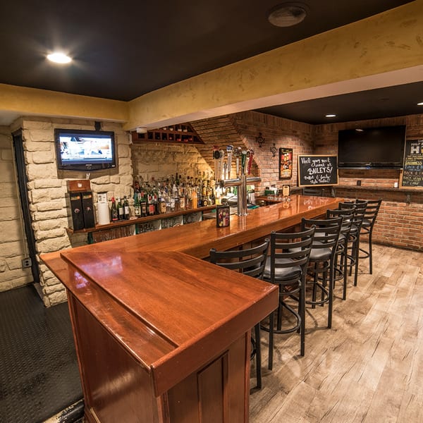 Bailey's Smokehouse bar with a long wooden counter, bar stools, brick walls, and a TV.